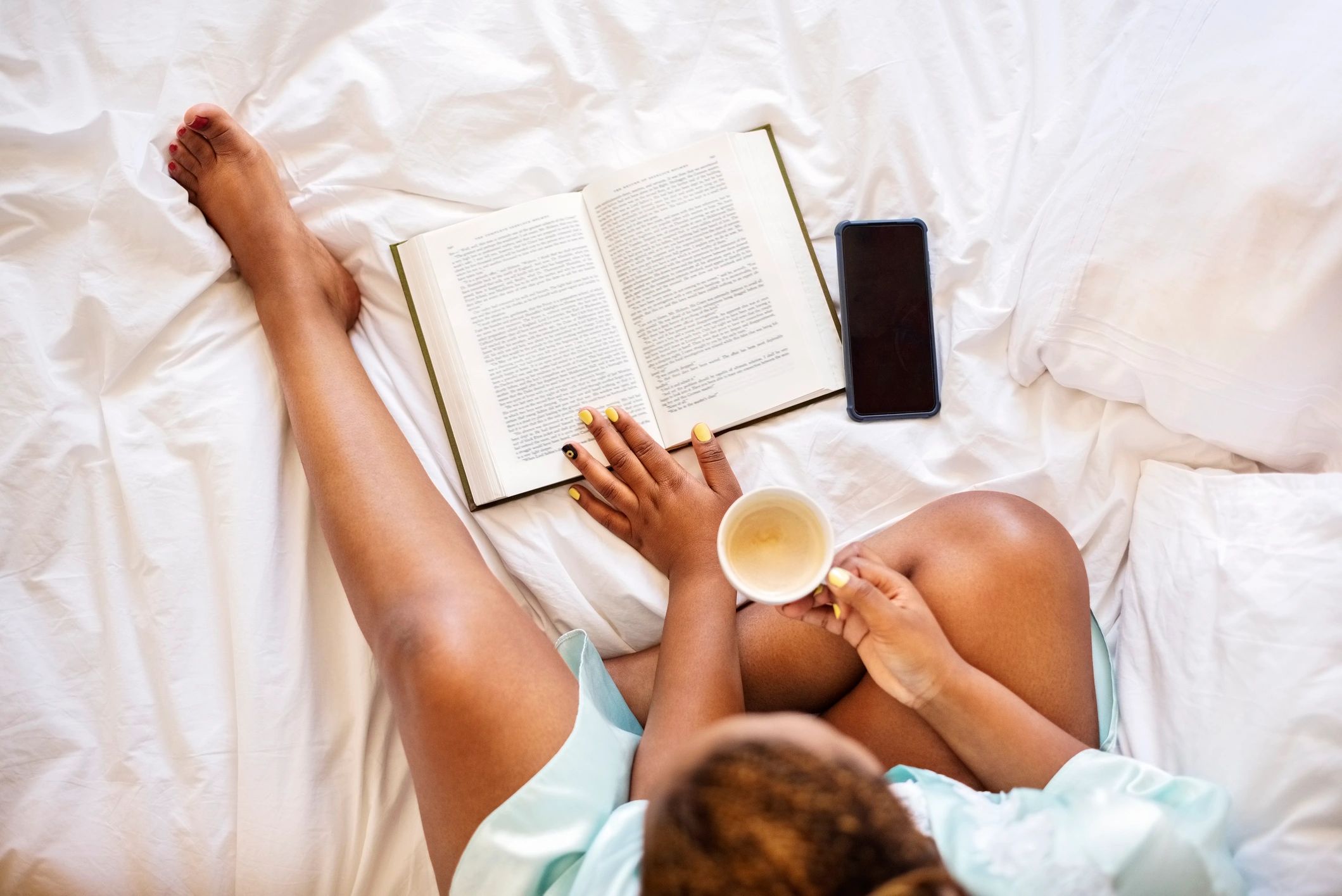 Woman reading in bed with a warm drink in the morning