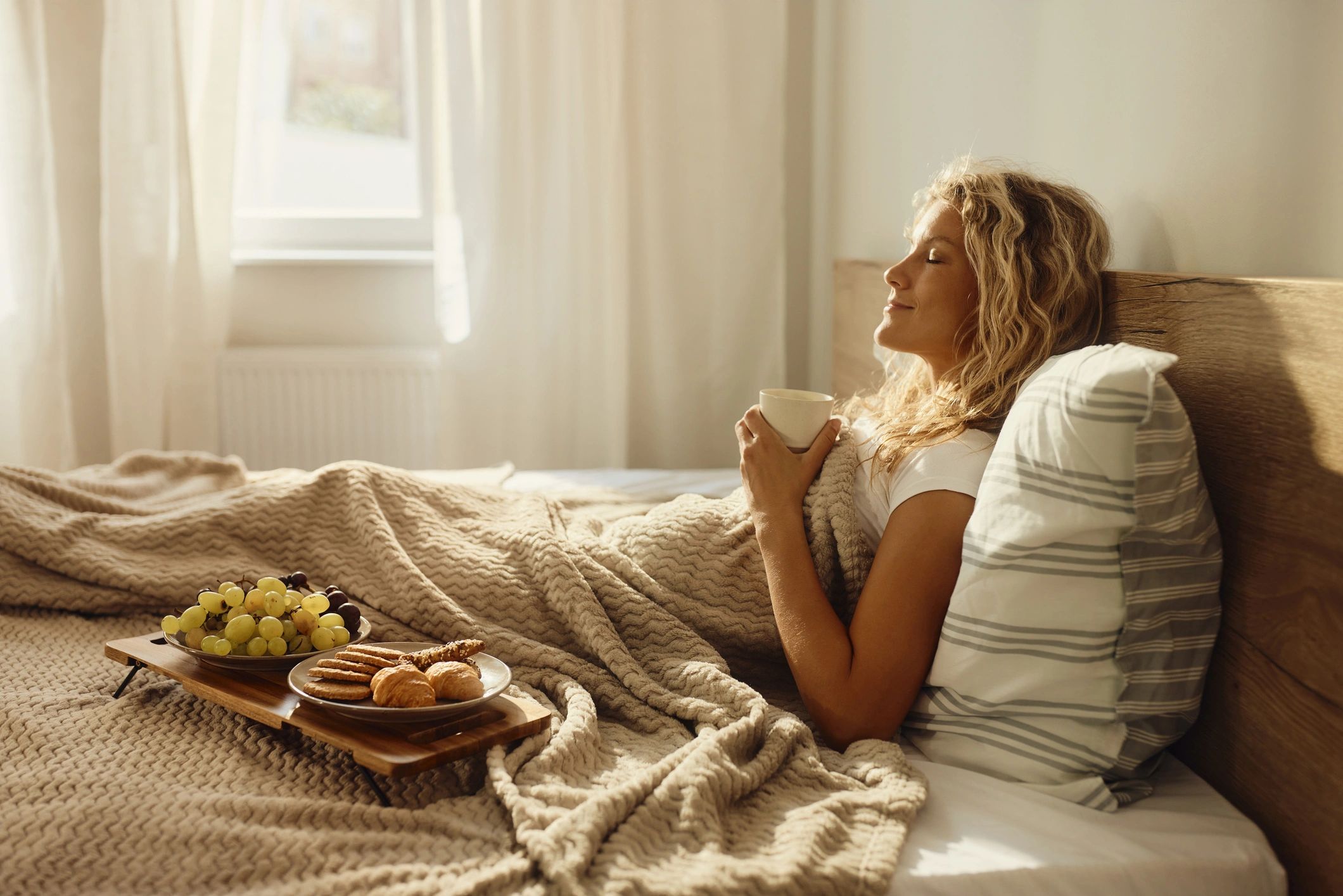 Woman relaxing in bed with morning coffee, eyes closed