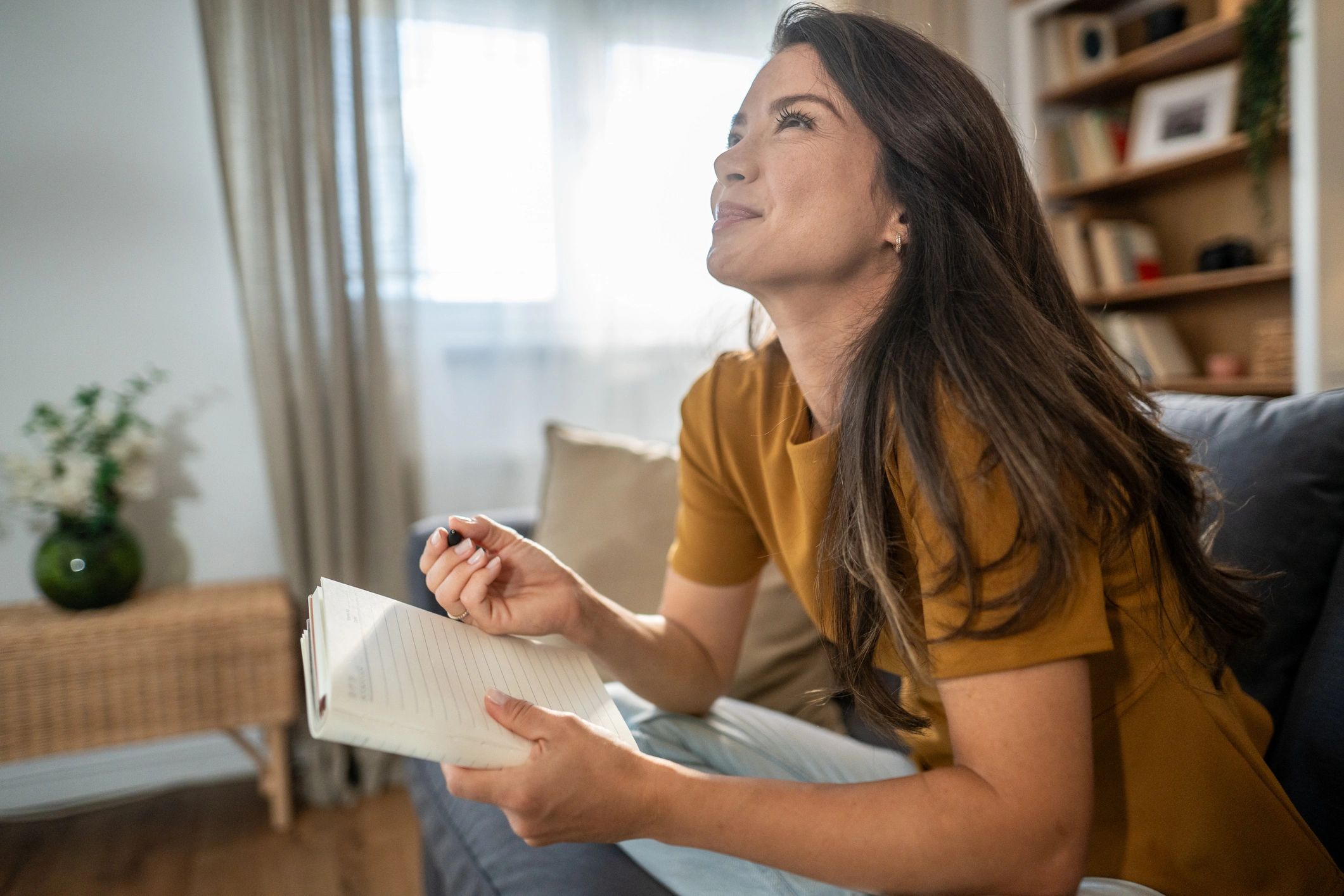 Woman journaling on a sofa in warm sunlight
