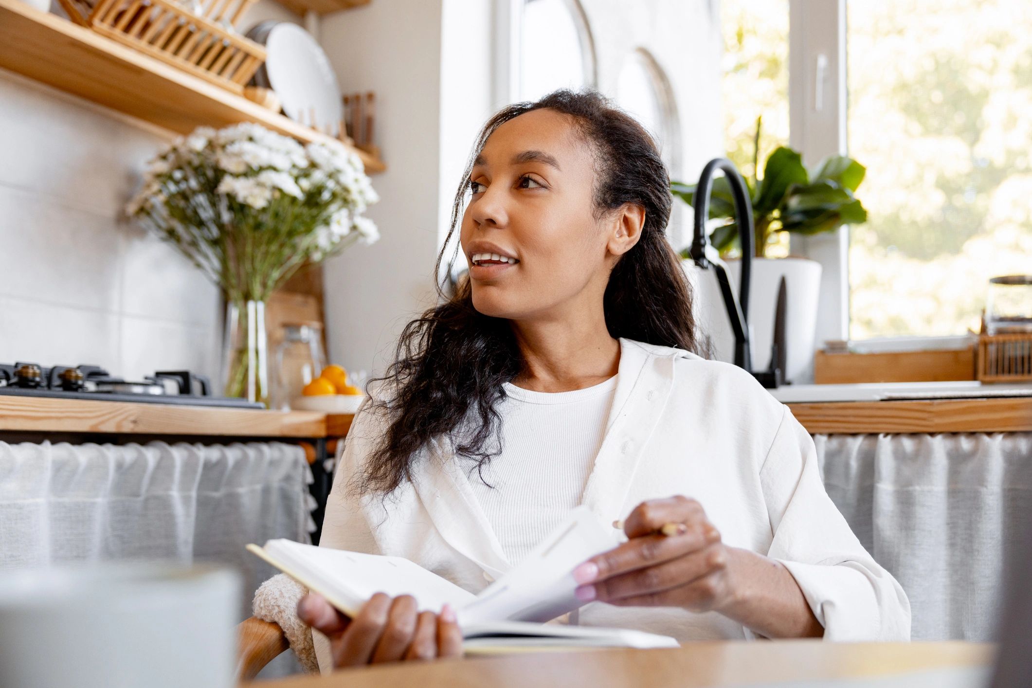 Woman journaling at a sunlit kitchen table, planning a supportive routine