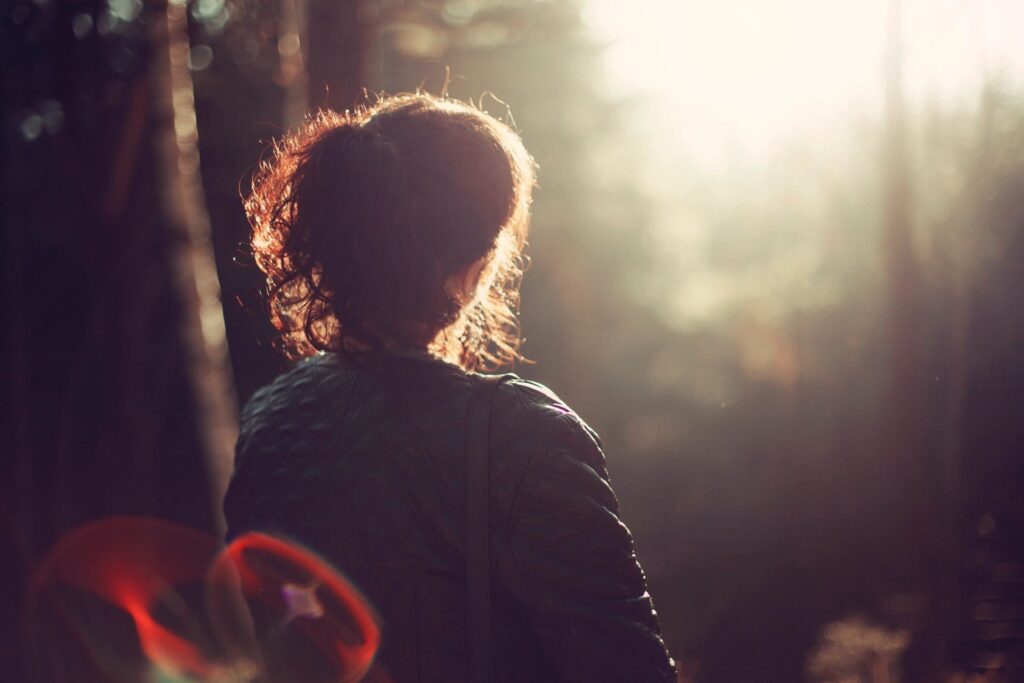 Woman with ponytail looking at bright light in a forest.